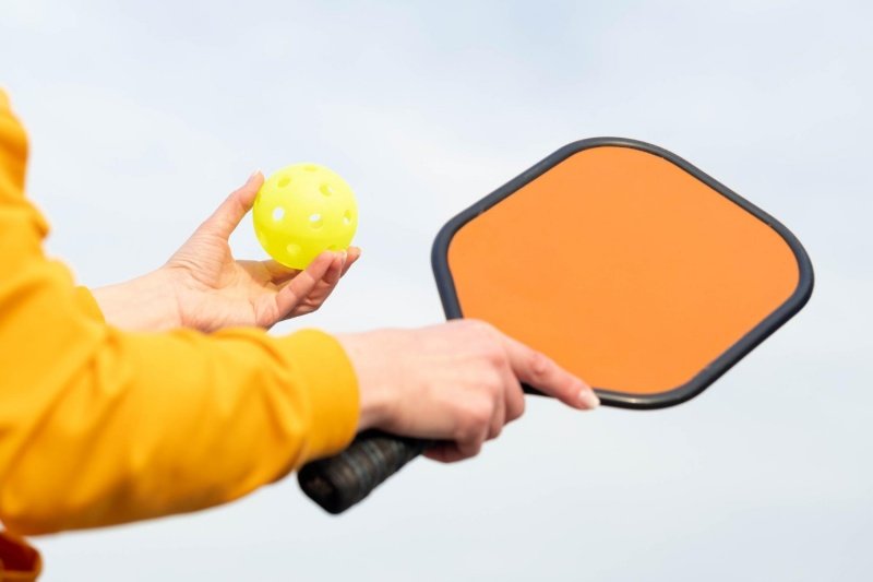 Close-up of orange pickleball paddle and ball in player’s hands