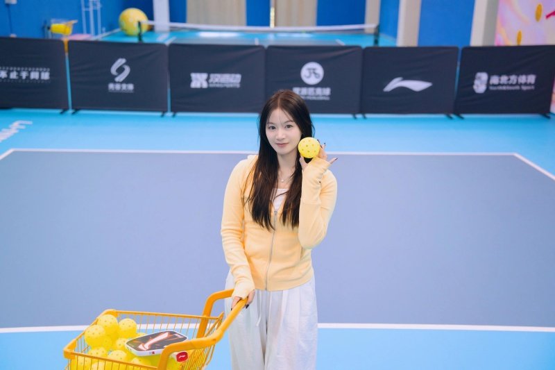 pickleball-court-yellow-balls Woman holding a pickleball ball and standing by a cart full of balls on the court