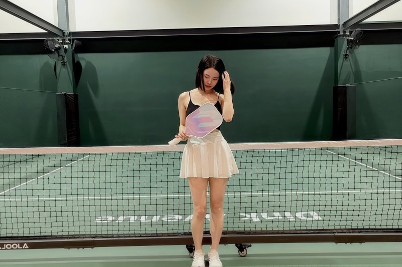 pickleball-net-posing Woman standing by the pickleball net holding a paddle