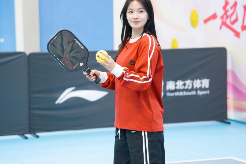 pickleball-red-shirt-ready Woman holding a pickleball paddle and ball, ready to play on the court