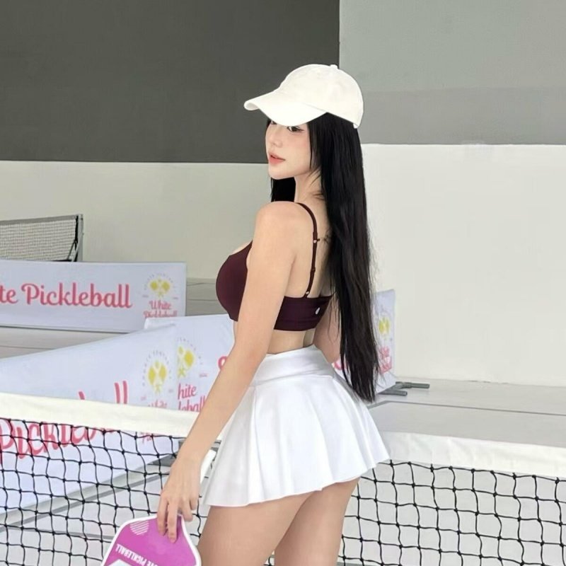 pickleball-court-player Female pickleball player holding pink paddle on court wearing white skirt and cap
